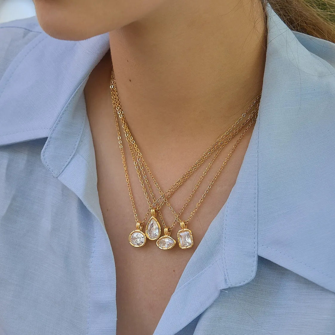 Four clear stone pendant necklaces layered together on a model