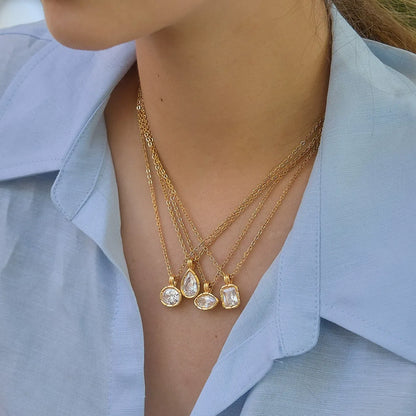 Four clear stone pendant necklaces layered together on a model