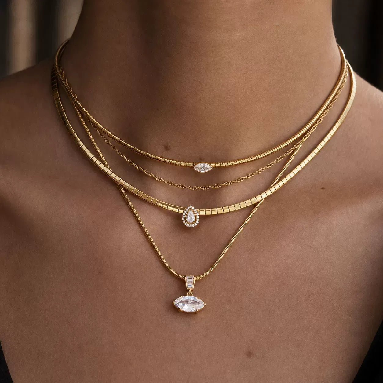 Layered snake chain necklaces with clear stone pendants worn on the neck